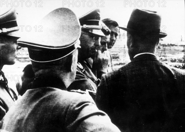 Himmler (center), chief of the ss visiting oswiecim (auschwitz) in 1942 accompanied by a group of ss officers, on right in civillian dress is faust of i,g, farben.