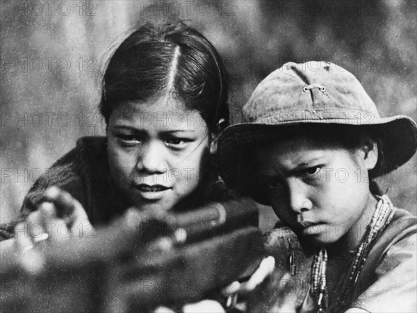 A fourteen year old viet cong girl teaching her younger brother to fire a rifle, thua thien province, south vietnam, 1968, vietnam war.