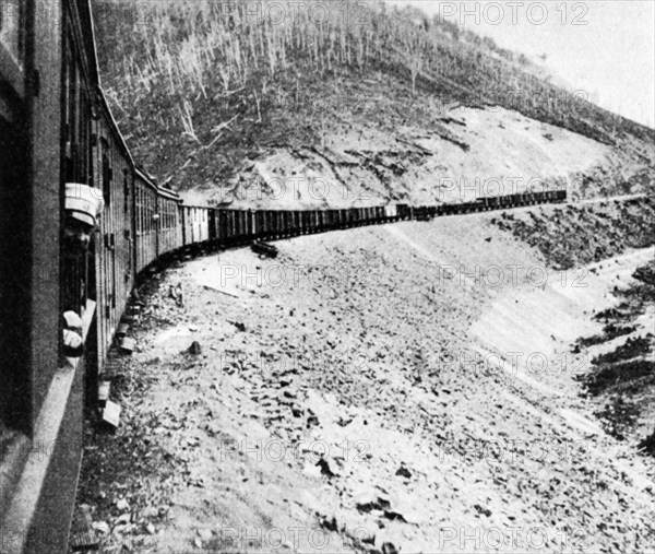 A man sticking his head out of a window of a railway car of a train traveling along the trans-siberian railroad in 1905, russia.