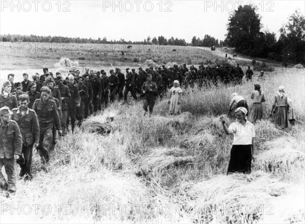 A soviet woman harvesting in a field torn by shells only a short time ago, shakes her fist at a line on nazi pows marching eastward under guard, feb,14, 1944.