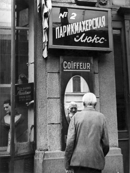 A peasant who came to moscow from the provinces, stops to look at himself in the street mirror of a barber shop,  his hair has been 'bobbed' as millions of peasants of former russia customarily trimmed their hair,  one seldom meets such a hair-cut these days when all make use of modern barber shops,  moscow, 1935, (credit: sovfoto/eastfoto).