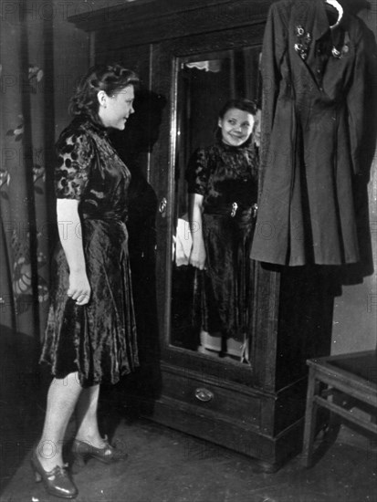 Nina lobkovskaya in war and peace, like all young girls, nina loves pretty clothes, here she is trying on a dress during a shopping trip, if it were not for her uniform with its decorations hanging nearby, no one would guess that she has been through the war, 1940s.