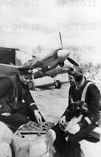 World war 2, two decorated soviet fighter pilots, senior lieutenant v, pokrovsky (left) and captain p, orlov, enjoying a game of checkers between missions, they have each shot down 10 enemy planes, an american p-40 is in the background (lend-lease).