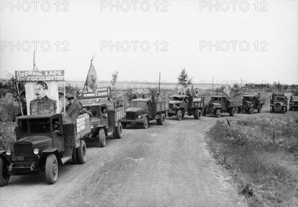 Harvest time on a collective farm in the ussr, august 1947, trucks from the stalin collective farm in the stavropol territory taking grain to the state elevator, the banner reads 'first bread goes to the state'.