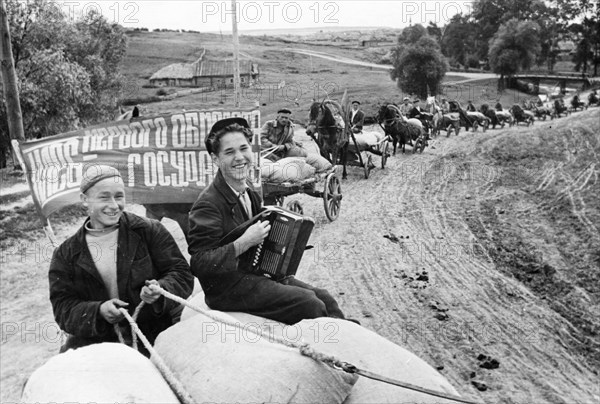 Harvest time on a collective farm in the ussr, august 1947, workers of the vakhitov collective farm taking grain to an elevator in the tatar autonomous soviet socialist republic, the banner reads 'bread from the first harvest goes to the state'.