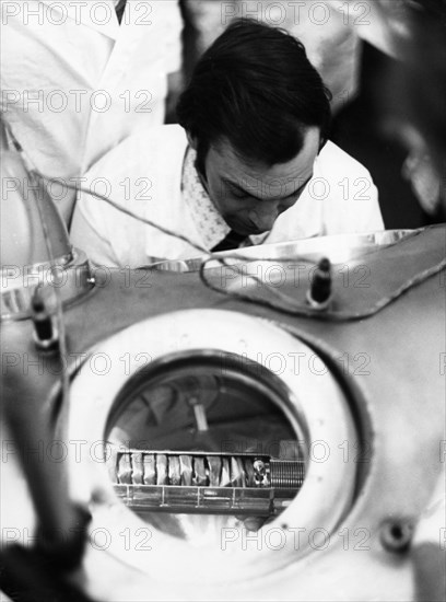 The ampule containing lunar soil and rock delivered by the re-entry module of the soviet lunar lander, luna 24, is being examined in a vacuum chamber by a scientist, it has been opened at the receiving laboratory of the ussr academy of sciences, 1976.