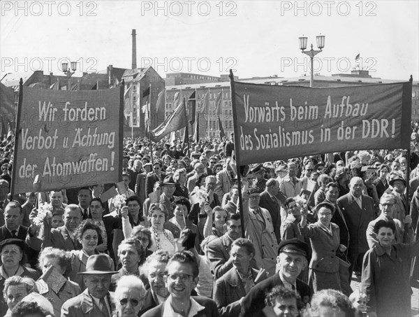 Berlin, gdr, may 1, 1957, berlin's working people marching across marx-engels square, the banners read 'we demand that atomic weapons be prohibited and outlawed!' (left) and 'forward with the building of socialism in the gdr!'.