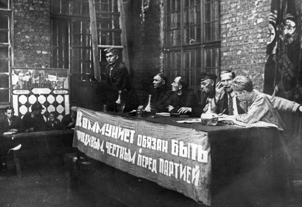 Comrade solovyov, the secretary of the communist party branch at the krasny putilovets plant, undergoing questioning duing the campaign to cleanse the cp of hostile elements, leningrad, 1933, the banner reads: 'a communist is obliged to be truthful and honest before the party'.