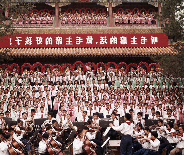 A mass chorus formed by peking (beijing) children singing the revolutionary song 'we are successors to communism' at chingshan park in celebration of  international labor day on may 1st (may day), the banner reads 'listen to chairman mao's words, be chairman mao's good children', 1965.