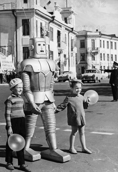 A robot belonging to local circus performer oleg sokol helping two children with balloons cross the street in arkhangelsk, ussr, 1967, the robot is part of the technical illusion attraction 'wonders without their wonders' that he performs at the circus.