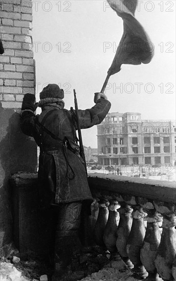 World war 2, battle of stalingrad, february 1943: a red army soldier raises the soviet flag (hammer and sickle) on the roof of a downtown stalingrad depatment store where the staff of field marshal von paulus was housed.