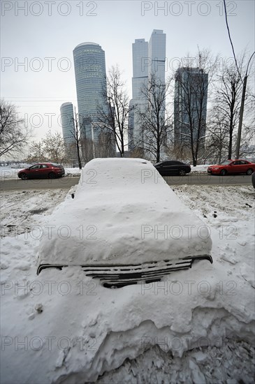 Moscow, russia, february 4, 2010, abandoned car buried in snow off a road, with the moscow international business centre (mibc) skyscrapers in the background, russia is launching a cash-for-bangers scheme in march 2010 to encourage motorists to scrap their used cars in favour of buying a new russian-made vehicle, the scheme gives drivers a 50000 rouble voucher to trade in cars that are more than 10 years old to buy a new model.