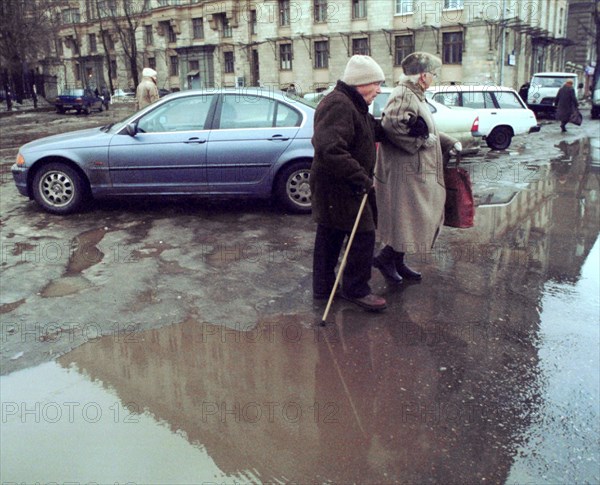 Moscow, russia, february 5, 2002, an old couple trying to cross a street on tuesday, after the recent thaw, with day temperatures reaching up to 4 degrees celsius, roads are covered with puddles of melting snow.