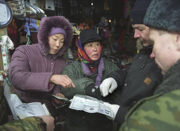 Policemen examine the papers of a chinese merchant at a vladivostok market, vladivostok,russia, january 17 2003, control of foreigners has been tightened because of crime growth in russia's maritime territory, in 2002, about 200 crimes in the region were committed by foreign citizens, which is by 10 per cent more than in the previous year.