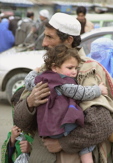 Kabul, afghanistan, march 22, 2003, a man with a child pictured in a street of kabul, servicemen of kabul security department have toughened control here, checking all vehicles arriving to the afghan capital and passengers' documents, authorities of the country fear that strike on iraq can destabilize situation in afghanistan.