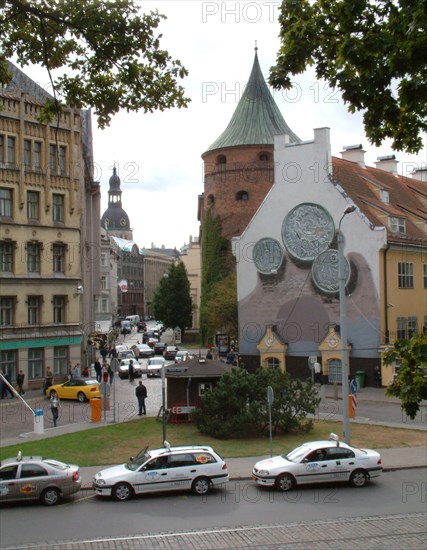 Smilsu street, a business area in old riga, latvia, the powder tower (r) and the dom cathedral (in the background), the coins depicted on the right part of the building are lats, the modern latvian currency, in the foreground are riga taxi cabs.