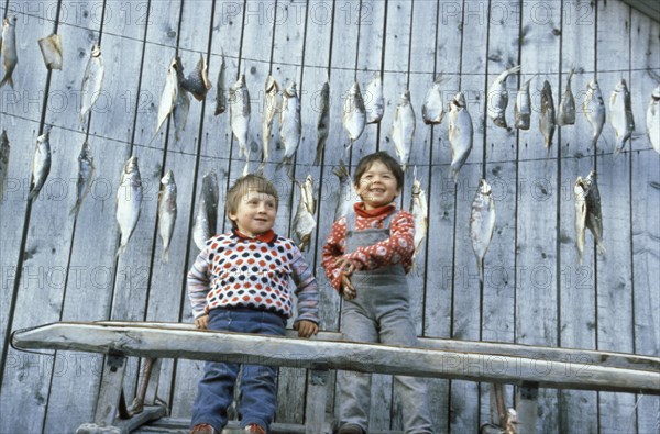 Two boys in front of a house with drying fish in th irkutsk region of siberia, 1990s.