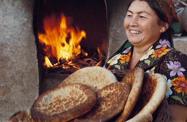 Uzbek woman with freshly baked loaves of bread from the tandyr (uzbek oven), namangan, uzbekistan.