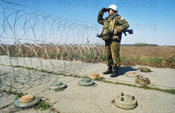 A russian un peacekeeping soldier standing watch on a road barricaded with razor wire and landmines in yugoslavia, april 1994.