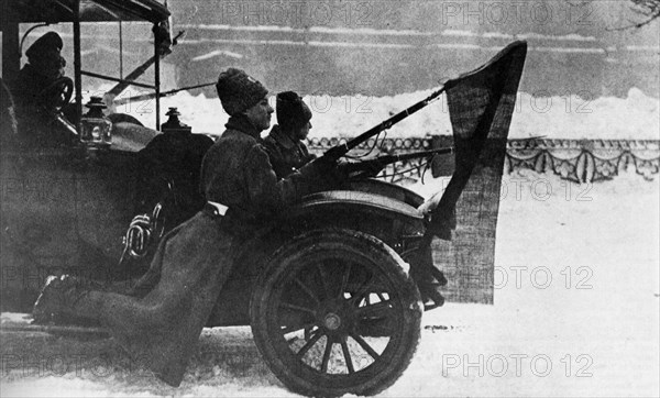 Soldiers traveling on the mudguard auto with red flags fixed to their bayonets. Pietrograd. 1917