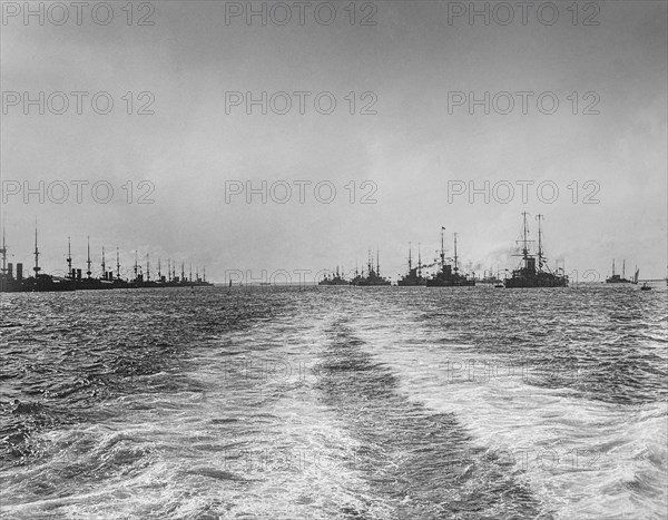 Black and white image of a wake in the ocean water from a nautical vessel and silhouetted ships