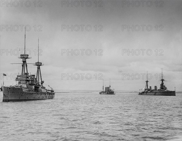 Black and white image of ships moored in the ocean under a cloudy sky