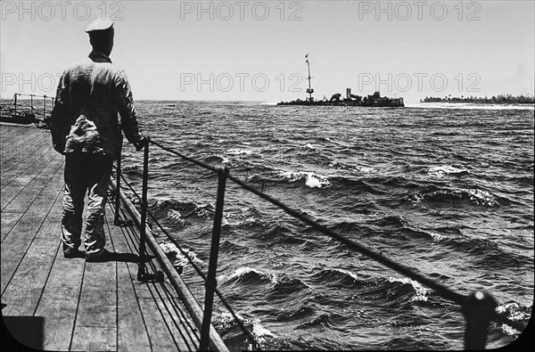 World war one image of a man standing on a ship's dock watching a another ship run aground