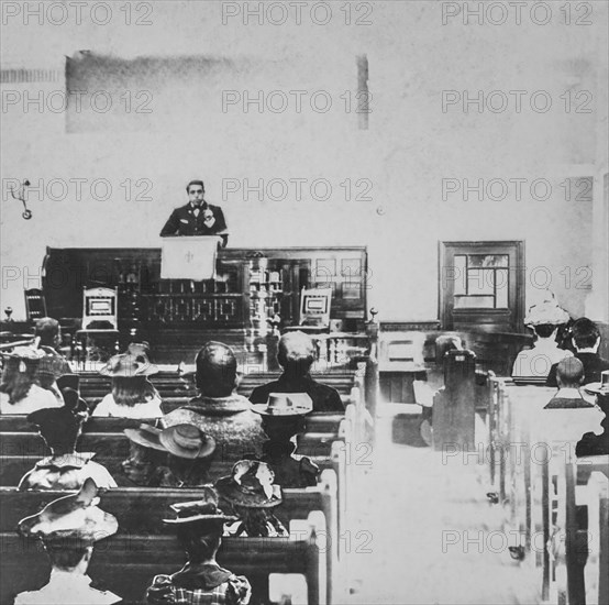 Black and white historic image of a preacher in a pulpit and the congregation in the wooden pews