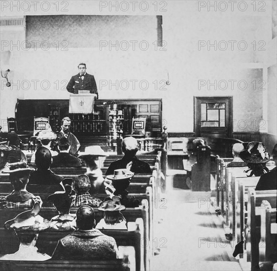 Black and white historic image of a preacher in a pulpit and the congregation in the wooden pews
