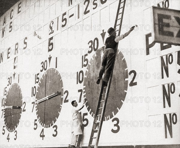 Men on ladders painting a small section of the largest tote board in the world