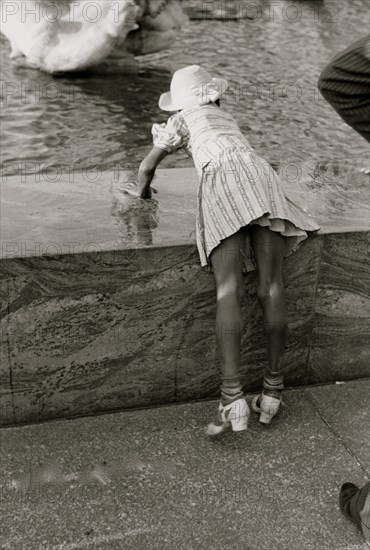 African American Girl leans over fountain pool to play with water