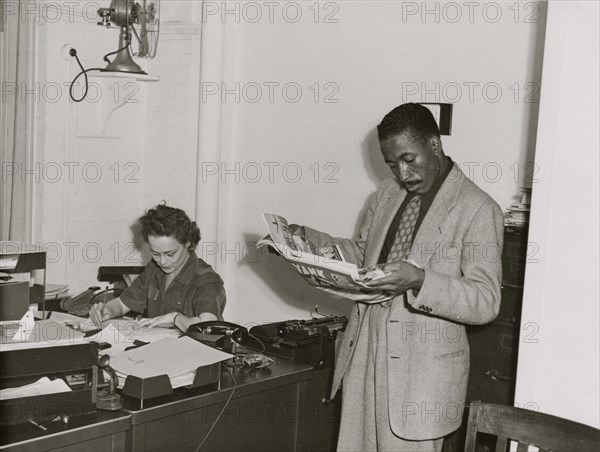 Gordon Parks, Farm Security Administration/Office of War Information photographer, standing in office with Helen Wool seated at desk