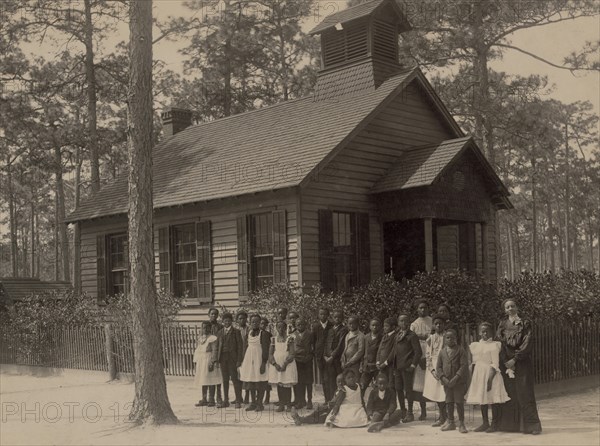 African American school children posed with their teacher outside a school, possibly in South Carolina