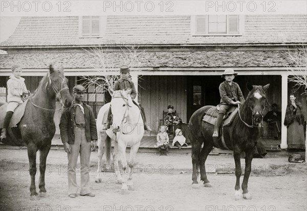 Afro-American enlisted man standing by three officers' children on horseback, Fort Verde, Arizona