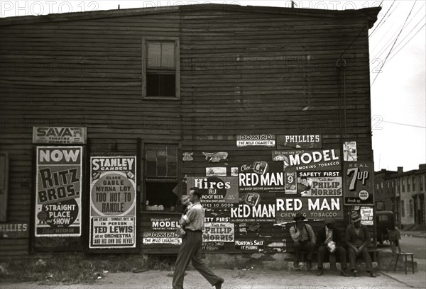 African American Men sit outside of retail establishment watching a  man walks by holding an infant