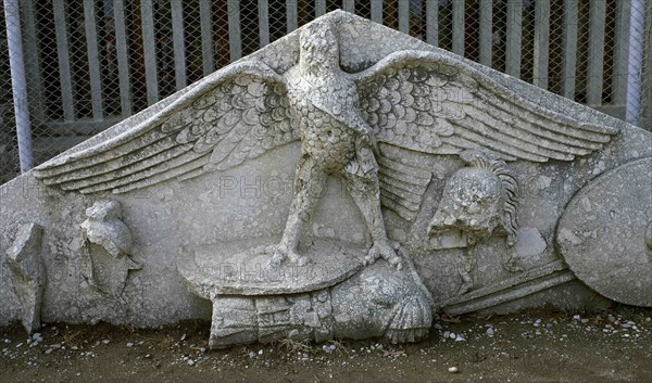 Eagle figure, armor, spear, helmet and circular shield at a Roman gable.