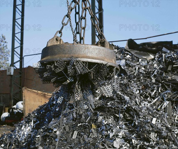 Electromagnet on crane lifting metal at scrap yard.