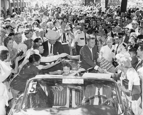 Senator John F. Kennedy (right) and Senator Lyndon B. Johnson (left with hat), along with Senator Kennedy's mother Rose Kennedy (center, seated in car), are greeted by supporters as they leave Burnett Park enroute to Dallas, Texas. The two were in the State campaigning for the presidential and vice presidential post of the US on the Democratic ticket. Fort Worth, Texas, 1960.