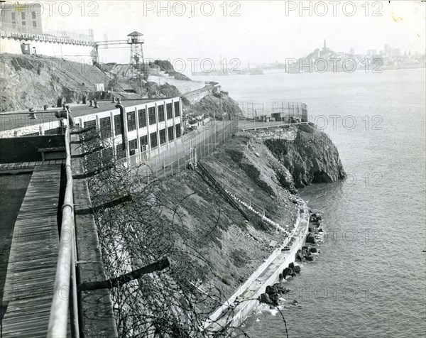 Alcatraz Prison, San Francisco, CA, circa 1940 - A view of the island taken from the industrial area with a guard tower, main cellhouse and San Francisco skyline in the background.