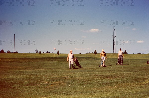 Men on the fairway of a golf course carrying their golf bags circa 1957-1960.