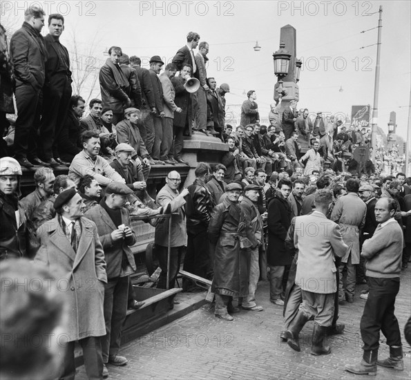 Construction workers demonstrate against the dismissal of 17 workers. the workers stand on the bridge railing of the Amstel Bridge opposite the building of the Nederlandse Aannemersbond Date April 9, 1964 / Location Amsterdam, Noord-Holland.