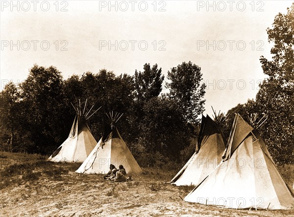 Edward S. Curtis Native American Indians - An Assiniboin camp containing four tepees with Indians seated on ground circa 1908.