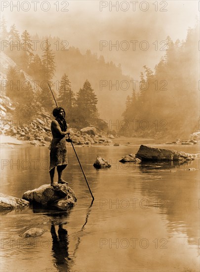 Edward S. Curtis Native American Indians - Hupa man with spear, standing on rock midstream circa 1923.