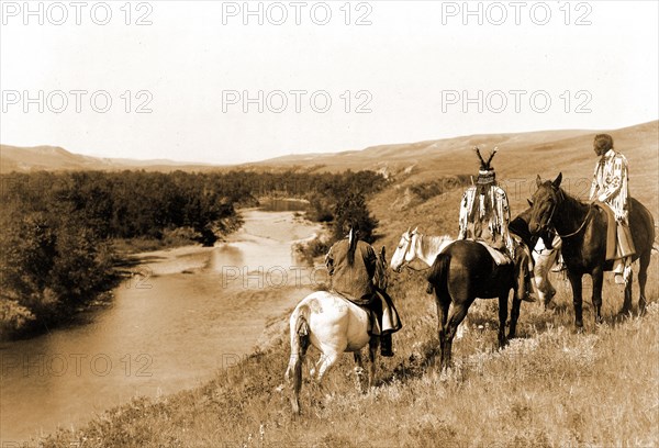 Edward S. Curits Native American Indians - Three Piegan Indians and four horses on hill above river circa 1910.