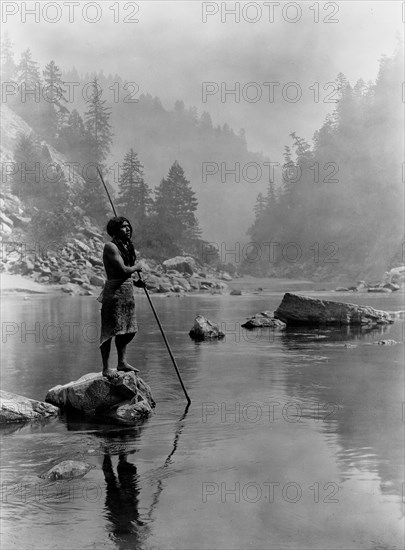 Edward S. Curtis Native American Indians - Hupa man with spear, standing on rock midstream circa 1923.