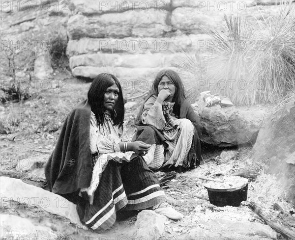 Edward S. Curits Native American Indians - Two Apache Indian women at campfire, cooking pot in front of one circa 1903.