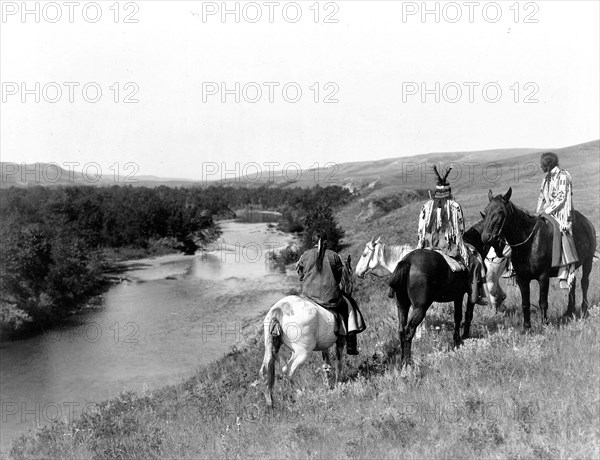 Edward S. Curits Native American Indians - Three Piegan Indians and four horses on hill above river circa 1910.