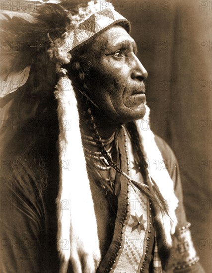 Edward S. Curtis Native American Indians - Raven Blanket, wearing several necklaces and warbonnet with ermine streamers circa 1910.