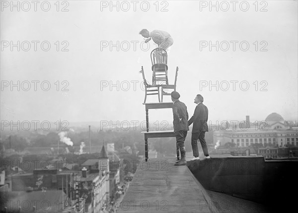 J. Reynolds Acrobat, performing acrobatic and balancing acts on top of building above 9th Street NW in Washington D.C. circa 1917.