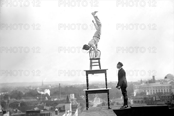 J. Reynolds Acrobat, performing acrobatic and balancing acts on top of building above 9th Street NW in Washington D.C. circa 1917.